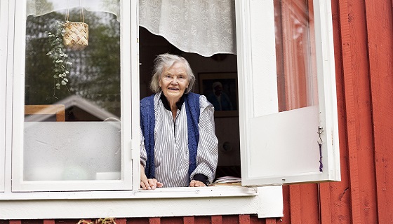 En äldre dam tittar ut genom ett fönster.