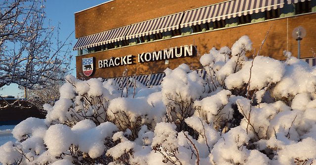 Foto på Bräckes kommunhus, snö på grenar i förgrunden.