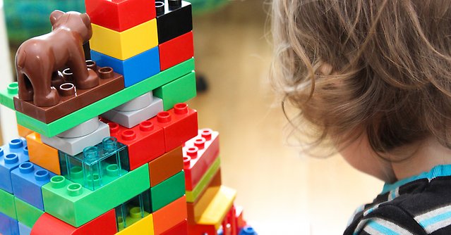 Bild på ett barn bakifrån bredvid ett torn byggt av lego-klossar